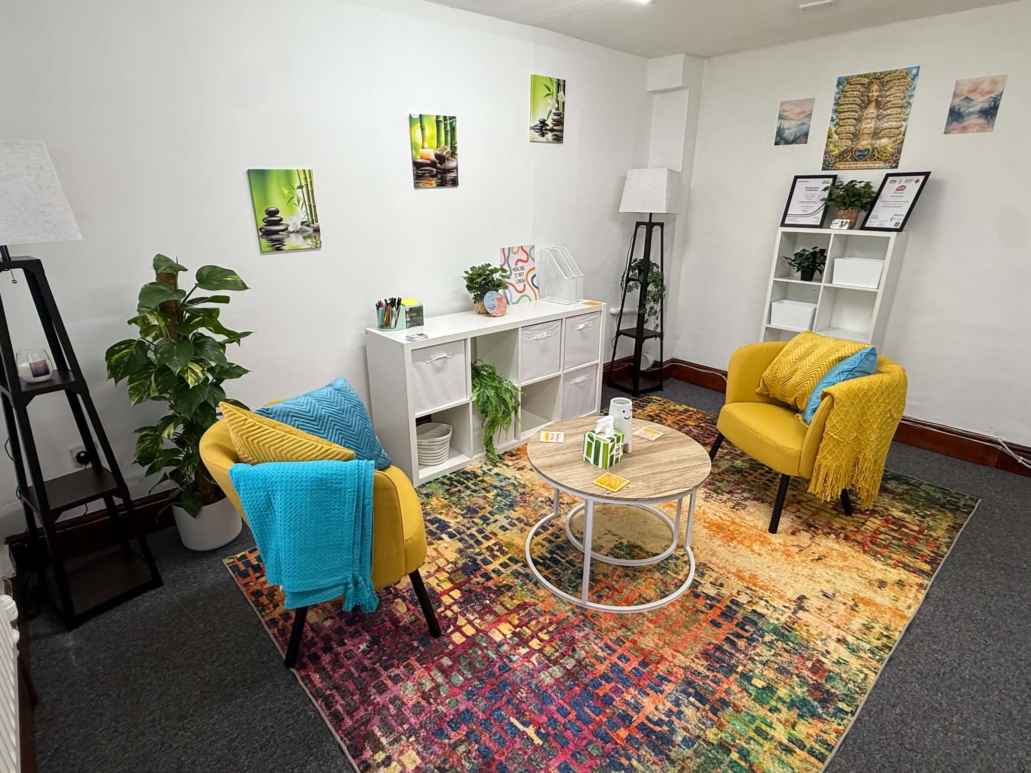 The counselling room, with two mustard-yellow armchairs, blue cushions and throws, plants and a round table on a colourful rug
